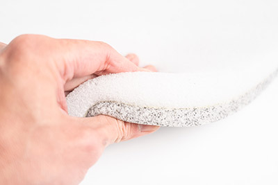 Hands pressing down on the foam. The bottom foam is grey and the top foam is white.